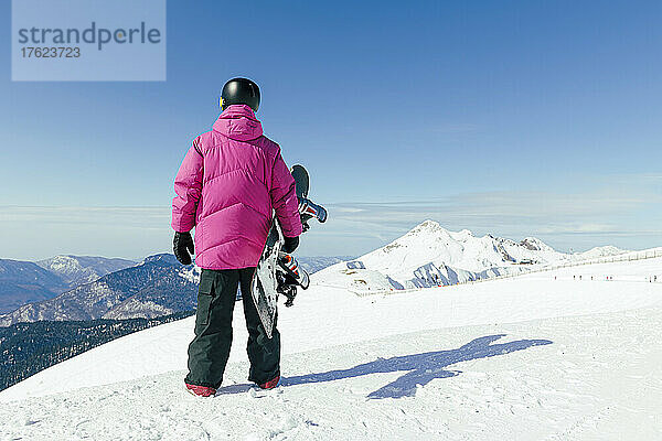 Mann mit Snowboard steht auf verschneitem Berg