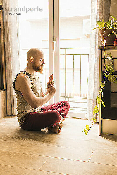 Mann meditiert zu Hause im Wohnzimmer