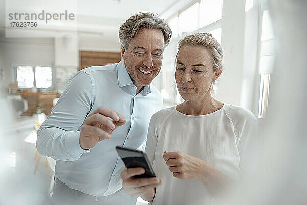 Geschäftsfrau teilt Smartphone mit lächelndem Geschäftsmann im Büro