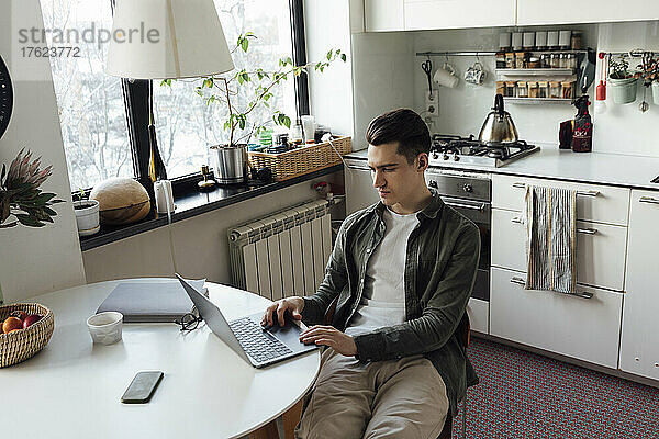 Junger Freiberufler nutzt Laptop am Tisch in der Küche