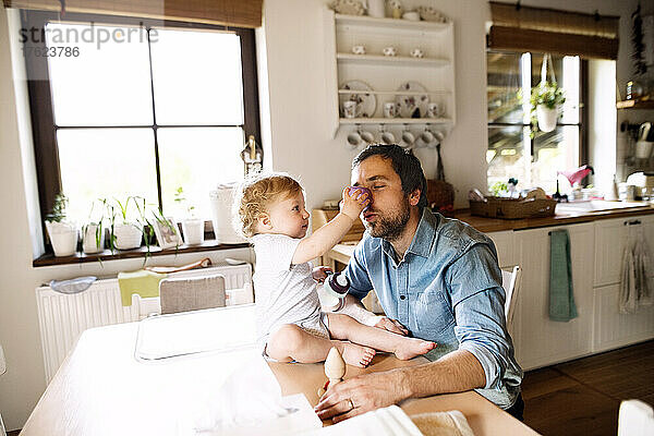 Father having fun with little boy sitting on kitchen table