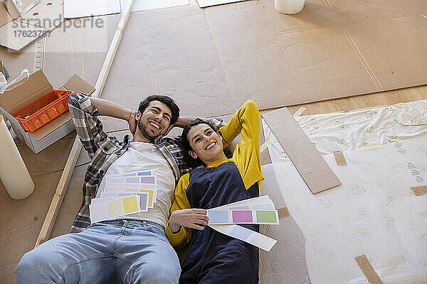 Ein glückliches Paar träumt vom Tag mit Farbmustern  die im neuen Wohnzimmer auf dem Boden liegen