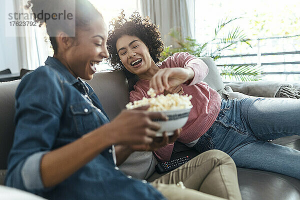Fröhliche Freunde genießen Popcorn zu Hause auf dem Sofa
