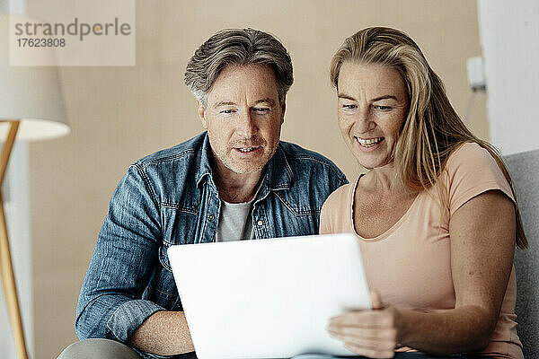 Smiling woman holding laptop sitting with man at home