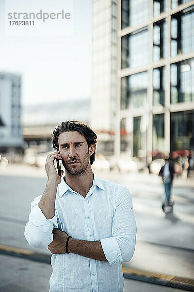 Hübscher Geschäftsmann  der am Fußweg mit dem Smartphone spricht