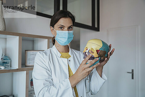 Arzt mit schützender Gesichtsmaske hält menschlichen Schädel in der Klinik