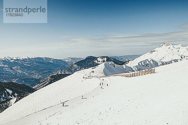 Menschen beim Skifahren in den verschneiten Bergen im Skigebiet an einem sonnigen Tag