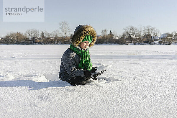 Junge mit warmer Kleidung sitzt im Schnee