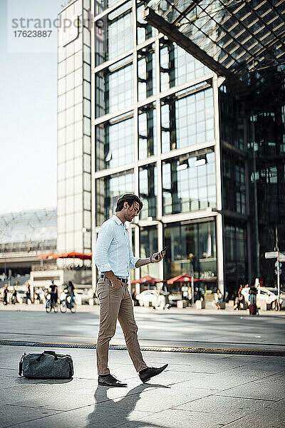 Geschäftsmann benutzt Smartphone und läuft mit der Hand in der Tasche auf dem Fußweg
