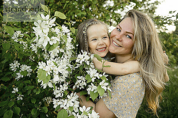 Glückliche Mutter mit süßer Tochter  die am blühenden Busch steht