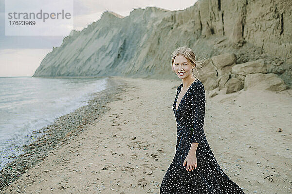 Glückliche Frau im Kleid steht am Strand