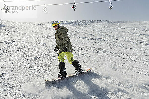 Junger Mann beim Snowboarden auf schneebedecktem Berg