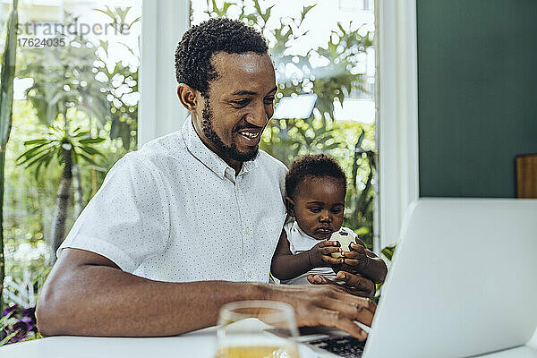 Lächelnder Vater und Sohn benutzen Laptop im Esszimmer