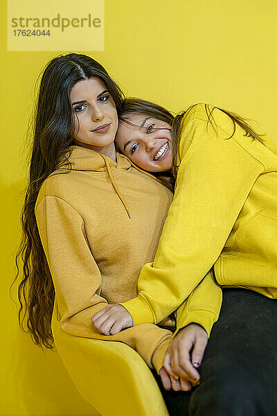 Happy friends in yellow hooded shirts sitting together at studio