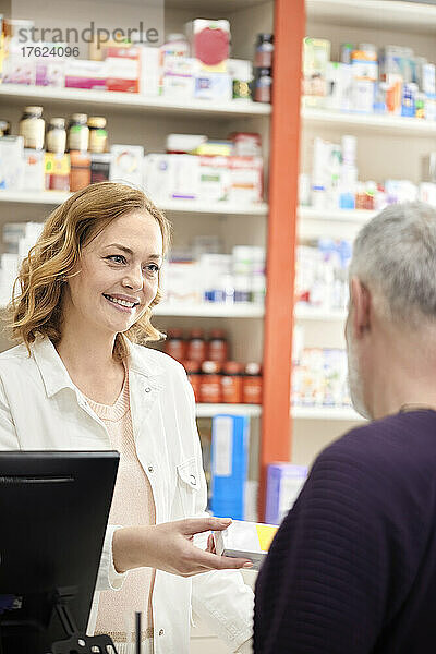 Lächelnde Apothekerin  die dem Kunden an der Kasse Medikamente gibt