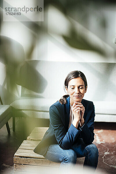 Geschäftsfrau sitzt mit geschlossenen Augen auf einer Holzkiste im Büro