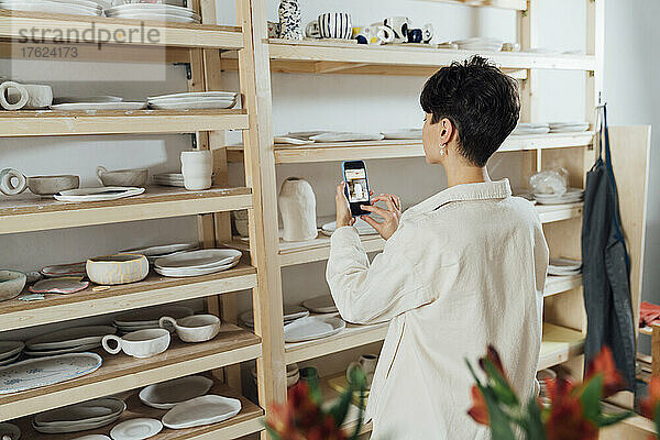 Unternehmer fotografiert Keramiktopf mit Smartphone in Werkstatt