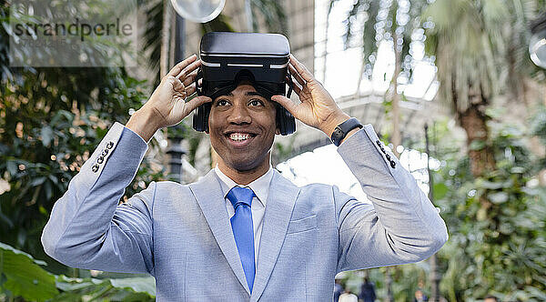 Glücklicher Geschäftsmann mit Virtual-Reality-Simulator  der neben Pflanzen steht
