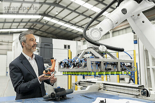 Geschäftsmann hält Roboterarmmodell in der Hand und untersucht Maschinen in der Fabrik