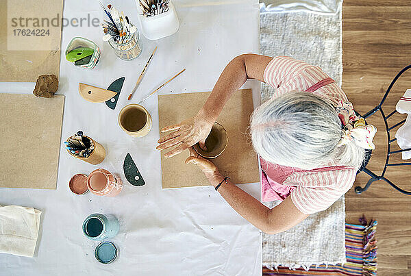 Woman making pot with clay sitting on chair at table