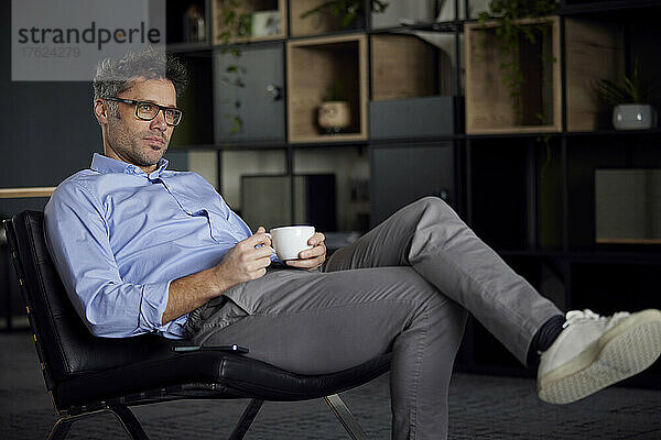 Geschäftsmann mit Kaffeetasse sitzt auf Stuhl im Büro