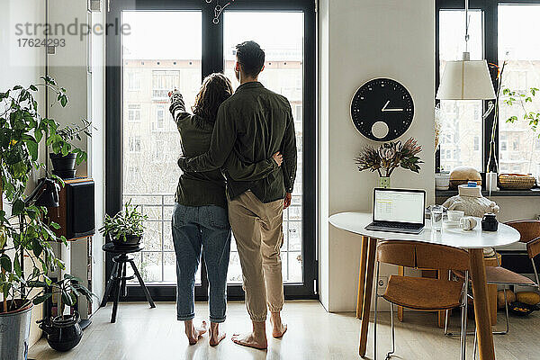 Junges Paar steht zu Hause mit den Armen am Glasfenster