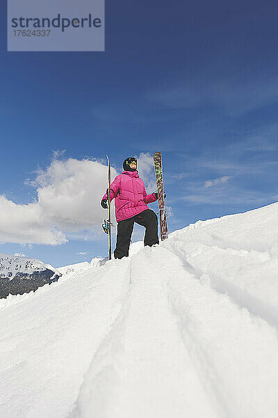 Mann in warmer Kleidung hält Ski und läuft auf Schnee