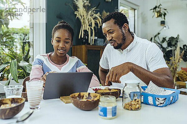 Vater und Tochter nutzen einen Tablet-Computer am Frühstückstisch