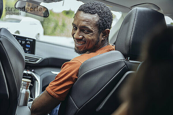 Lächelnder Mann  der im Auto über die Schulter schaut