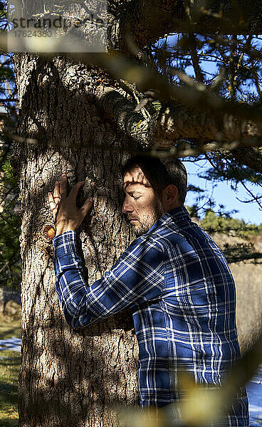 Mann mit geschlossenen Augen umarmt Baum