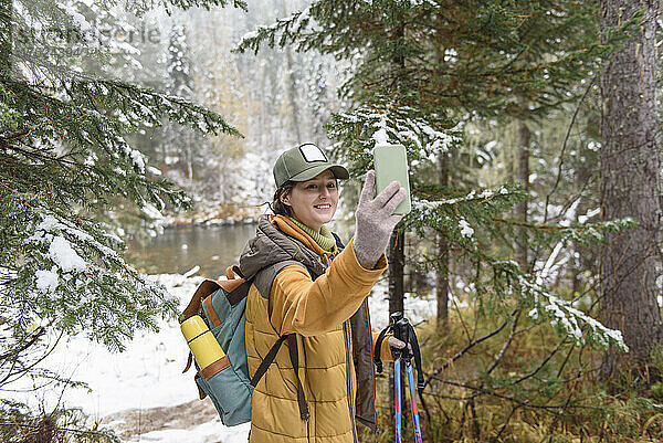Frau macht Selfie mit Smartphone und steht im Winterwald