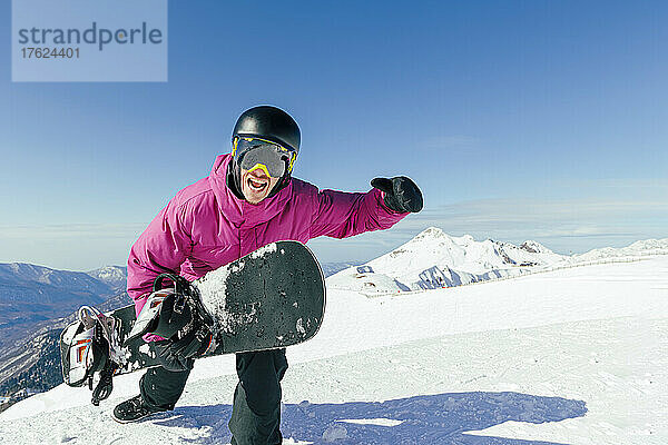Mann mit Snowboard schreit an einem sonnigen Tag auf einem verschneiten Berg