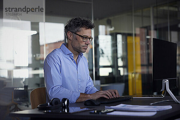 Geschäftsmann sitzt am Schreibtisch im Büro und nutzt einen Desktop-PC