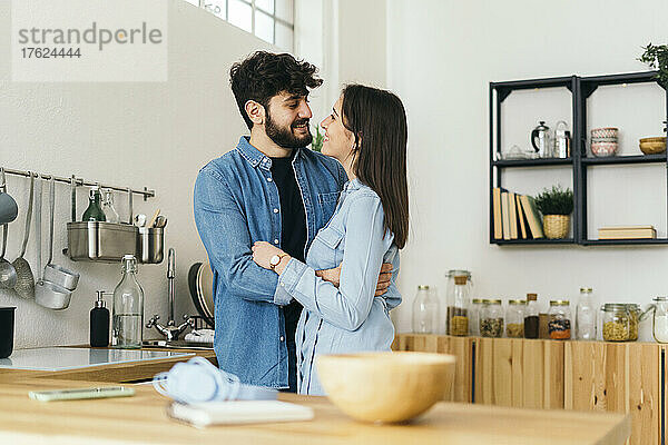 Lächelnder Mann umarmt Freundin  die zu Hause in der Küche steht