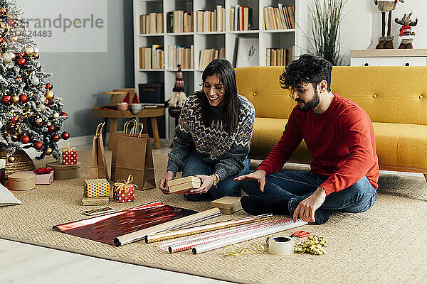 Glückliches Paar sitzt mit Weihnachtsgeschenken und Geschenkpapier zu Hause