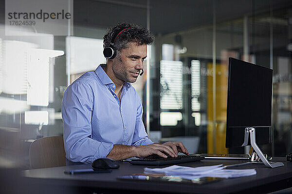 Geschäftsmann mit kabellosem Headset und Computer sitzt am Schreibtisch im Büro