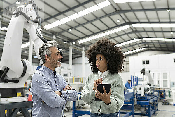 Ingenieur hält Tablet-PC in der Hand und diskutiert mit Entwickler in der Fabrik