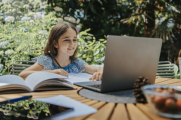Smiling girl e-learning through laptop at back yard