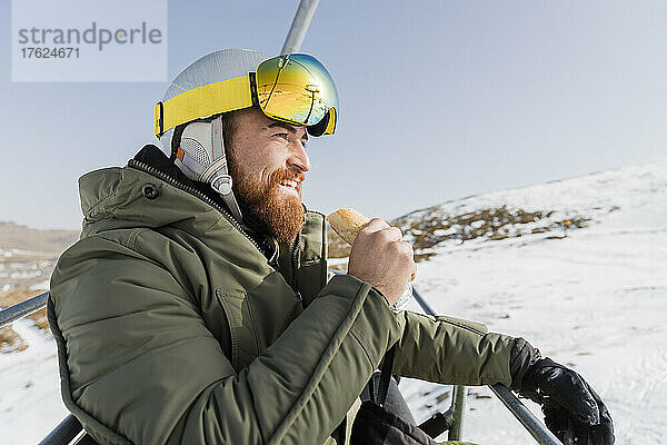 Lächelnder junger Mann isst Snack am Skilift