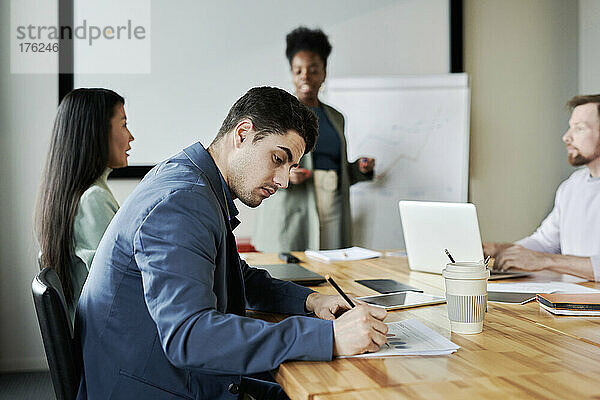 Junger Geschäftsmann macht sich Notizen  während er bei einer Besprechung im Büro am Schreibtisch sitzt