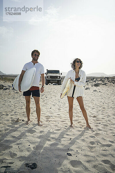Glückliches Paar steht mit Surfbrett am Strand