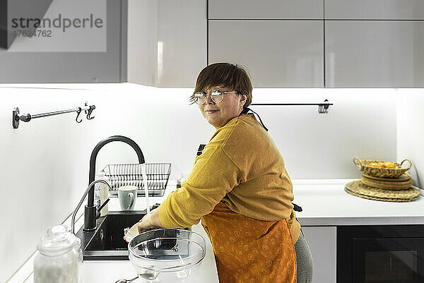 Ältere Frau spült zu Hause in der Küche Geschirr