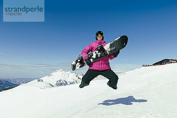 Glücklicher Mann mit Snowboard  der im Winter auf Schnee springt
