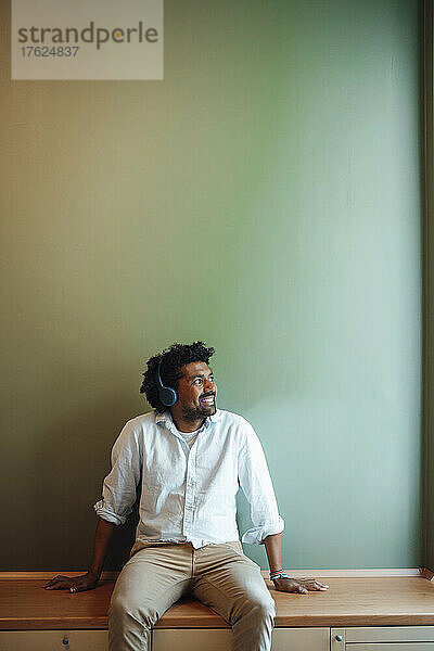 Smiling man listening music through headphones at home