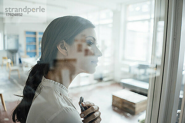 Geschäftsfrau hält Mobiltelefon durch Glaswand gesehen