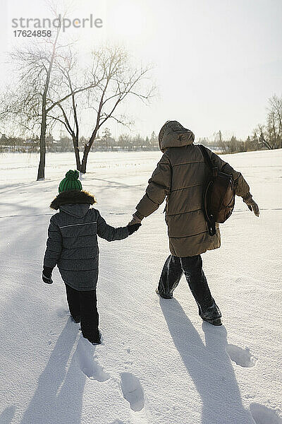 Mutter und Sohn halten sich an den Händen und gehen auf Schnee