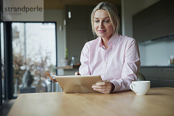 Frau sitzt am Tisch und benutzt Tablet-PC
