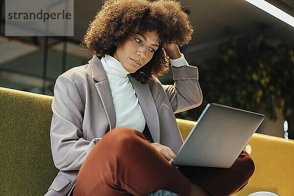 Berufstätige Frau mit der Hand im Haar und Laptop am Arbeitsplatz