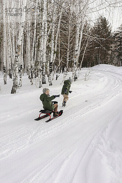 Jungen rodeln auf Schnee im Winterwald