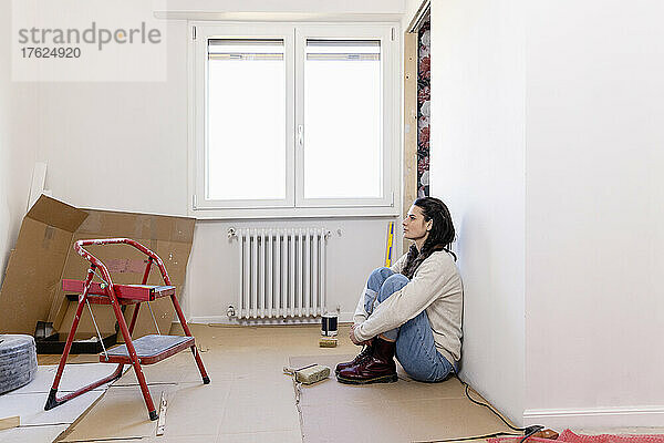 Nachdenkliche Frau sitzt bei Renovierungsarbeiten auf dem Boden